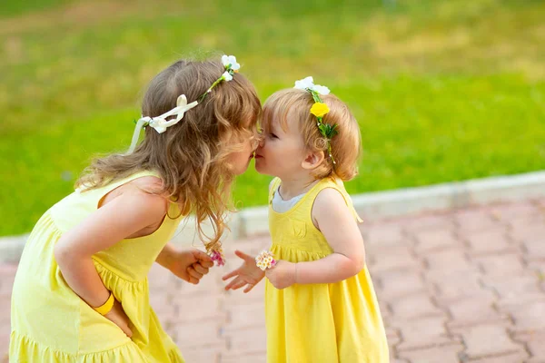 Dos hermanas en coronas de flores, vestidos amarillos besan — Foto de Stock
