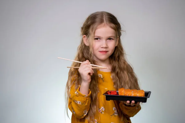 Little girl licks sushi sticks and keeps box rolls — Stockfoto