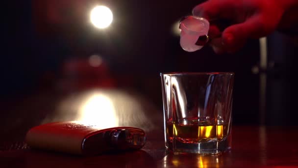 Кубик льоду кинутий у склянку віскі в темряві на барі — стокове відео