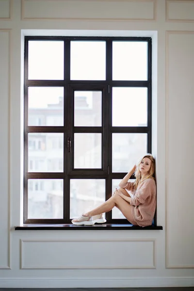 Hermosa chica rubia en suéter se sienta en la ventana —  Fotos de Stock