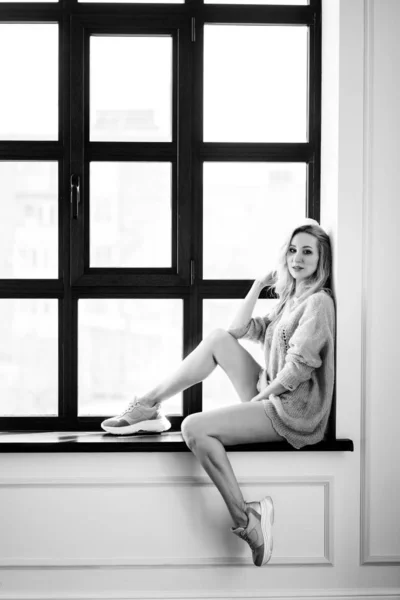 Una chica rubia en suéter se sienta en la ventana —  Fotos de Stock