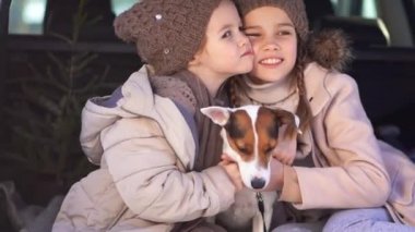Two sisters sitting in the trunk of a car with dog
