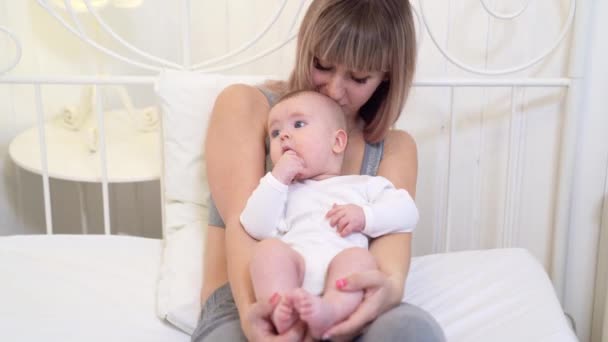 Mamá besa la cabeza del bebé sentado en la cama en casa — Vídeo de stock