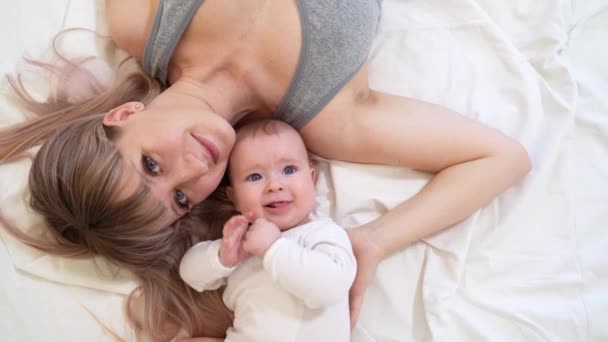 Mother with baby lying on bed mom kisses head boy. — Wideo stockowe