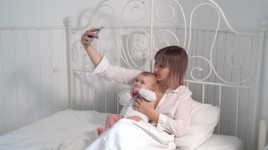 mum with baby bed taking selfies on smartphone