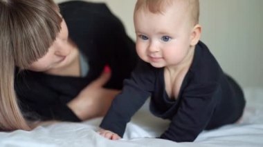 mother and son lying on bed. baby learns to crawl.