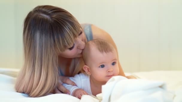 Madre e hijo acostados en la cama. bebé aprende a gatear . — Vídeos de Stock