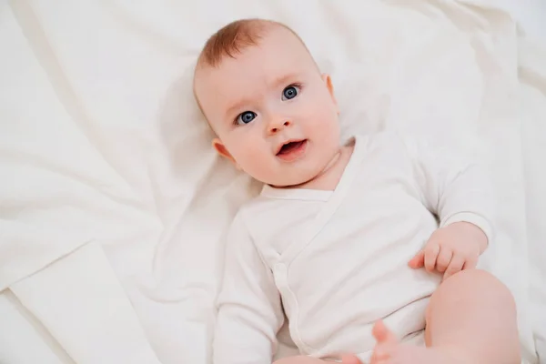 Bebê em roupas brancas deitado de costas na cama — Fotografia de Stock