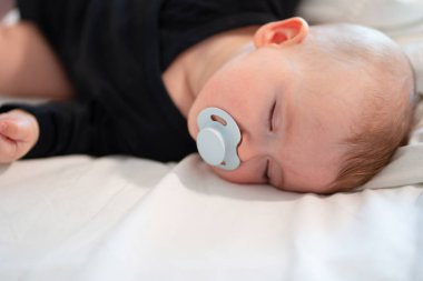 kid in black clothes with pacifier in mouth sleep