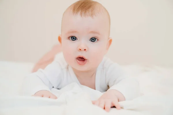 Bebé en ropa blanca acostado en la barriga en la cama —  Fotos de Stock