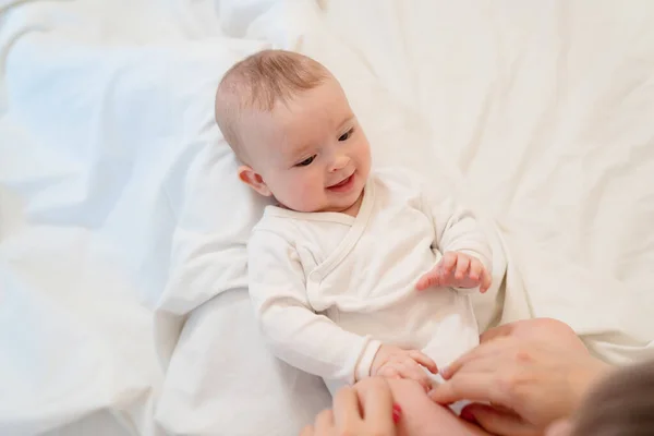 Baby i vita kläder liggande på rygg på sängen — Stockfoto
