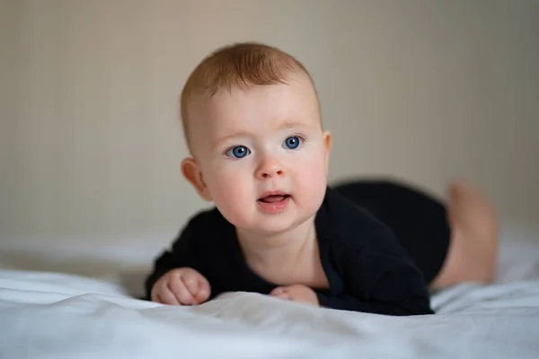 Bebé en ropa negra acostado en la barriga en la cama blanca —  Fotos de Stock