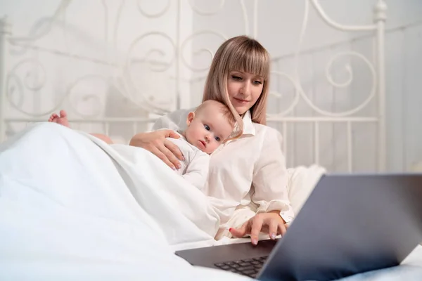 Madre en la cama con el bebé trabajando con el ordenador . — Foto de Stock