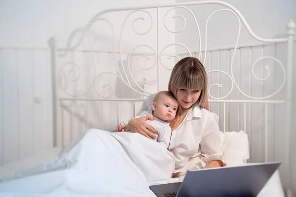 Madre en la cama con el bebé trabajando con el ordenador . — Foto de Stock