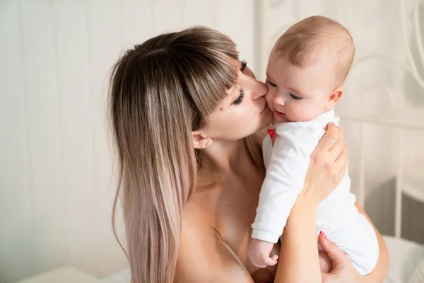 Mamá sentada en la cama con el bebé y besar a su hijo —  Fotos de Stock