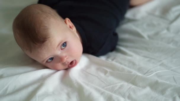 Малыш в черном лежит на кровати на белой кровати — стоковое видео