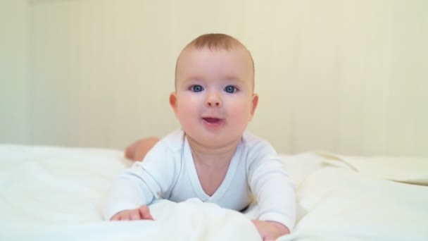Bebê em roupas brancas deitado na pança na cama — Vídeo de Stock