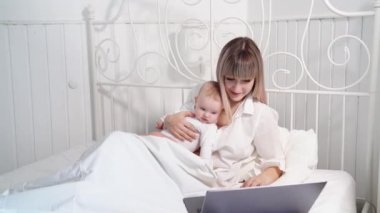 Mother in bed with baby working with computer.