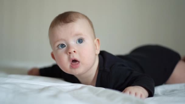 Bebê em roupas pretas deitado na pança na cama branca — Vídeo de Stock