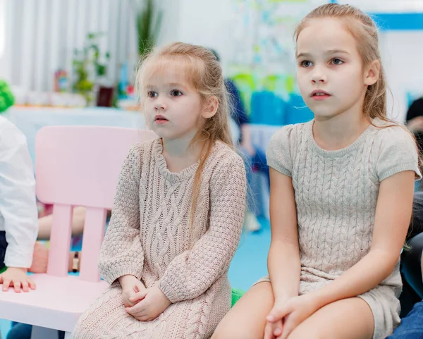 Two little girls sit on chairs and watch — Stock Photo, Image