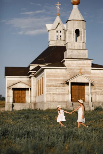 Meisjes houden elkaars hand vast en lopen tegen de houten kerk — Stockfoto