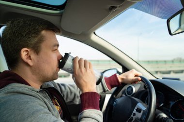 Gri kazaklı adam, arabanın direksiyonunda kahve iç. 