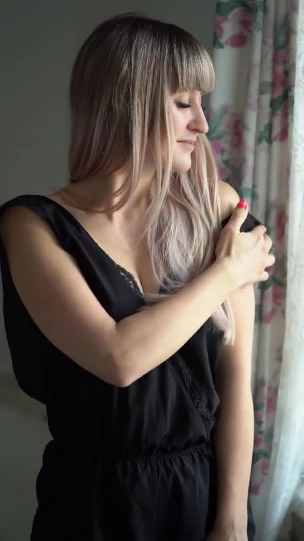 Дівчина, що стоїть біля вікна, знімає рукав з плеча — стокове відео