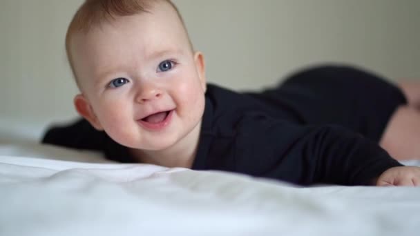 Baby schwarze Kleidung liegt auf Hinterleib auf weißem Bett — Stockvideo