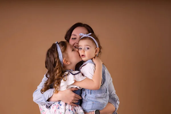 Zwei Schwestern im blauen Outfit küssen sich in die Arme der Mutter — Stockfoto