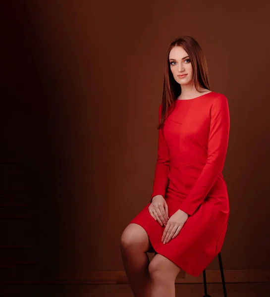 Menina bonita em vestido vermelho sentado em uma cadeira — Fotografia de Stock