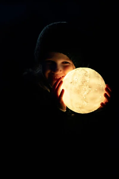 Little girl in cap and jacket holds a full moon — Stock Photo, Image