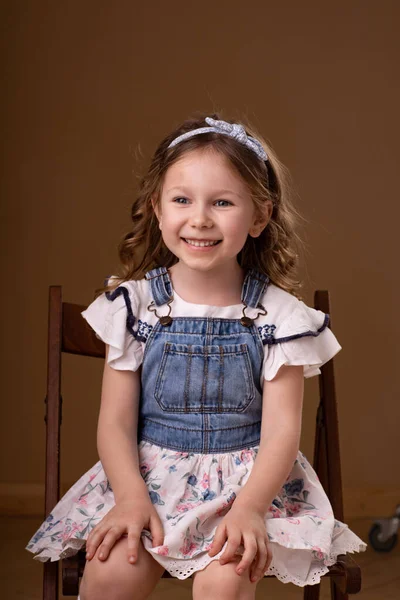 Kleines Mädchen mit Locken und Stirnband sitzt auf Stuhl — Stockfoto