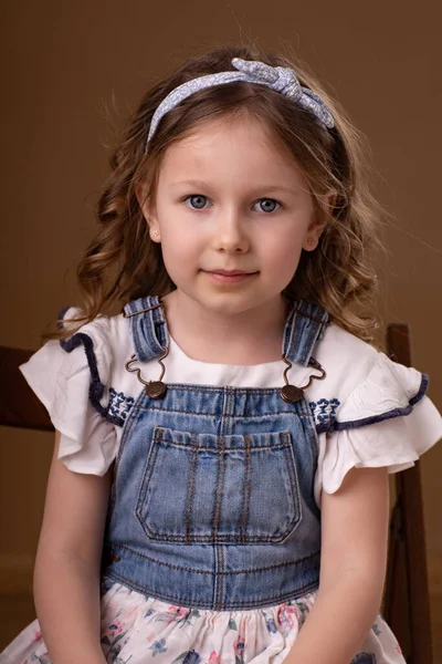 Kleines Mädchen mit Locken und Stirnband sitzt auf Stuhl — Stockfoto