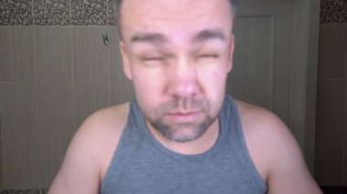 Tıraşsız adam banyoda yürüyor, gözlerini açamıyor.
