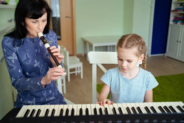 teacher teaches girl play synthesizer, plays flute