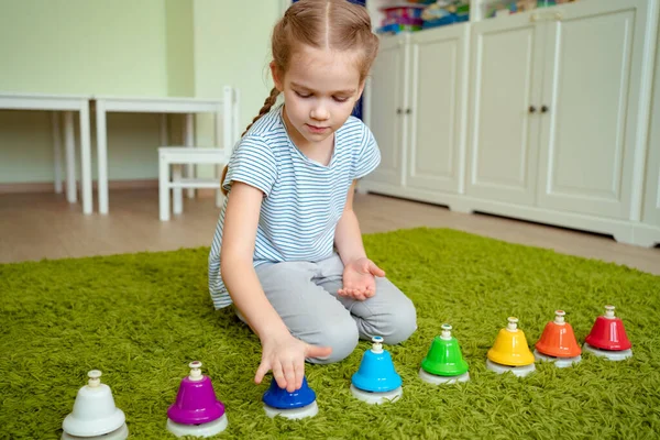 Liten flicka leker med färgglada musikaliska klockor. — Stockfoto