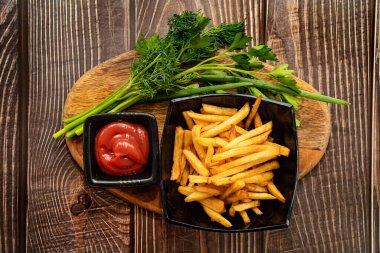 Siyah tabakta patates kızartması, yeşillik ve sos.