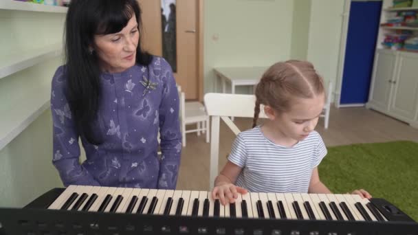 Leraar leert klein meisje spelen op synthesizer — Stockvideo