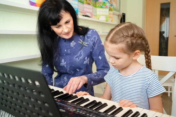 teacher teaches little girl to play on keyboard.