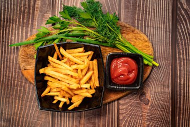 Siyah tabakta patates kızartması, yeşillik ve sos..