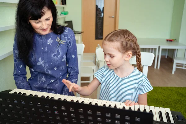 teacher teaches little girl to play on keyboard.