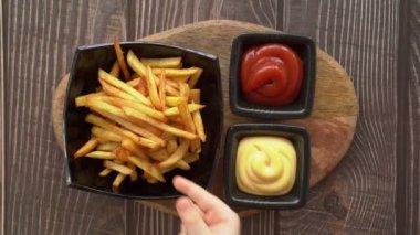 Elleri patates kızartmasını alır ve peynir sosuna batırır..