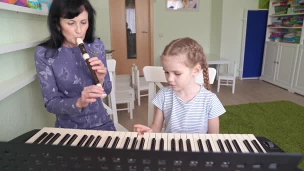 Woman teaches girl play synthesizer, plays flute — Stock Video