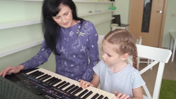 Teacher teaches little girl to play on synthesizer — Stock Video