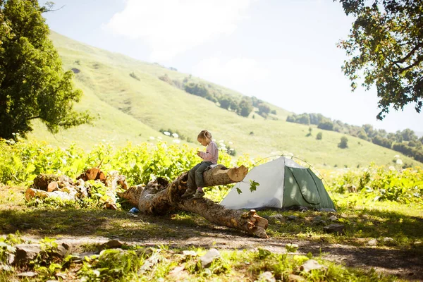 Küçük kız ağaçların kamp alanında dağlarda oturuyor.