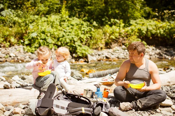 Pai com crianças em rochoso de rio de montanha e comer — Fotografia de Stock