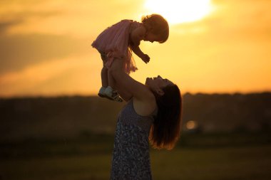 Siluetler gün batımında anne kız tarlasını fırlatıyor.