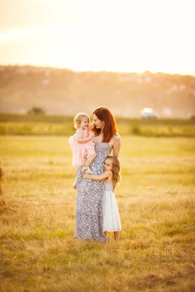 Mum with two daughters stand and hug mowed field — Stock Photo, Image