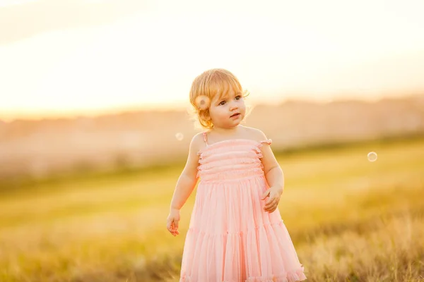 Kleines Mädchen beobachtet Seifenblasen bei Sonnenuntergang — Stockfoto