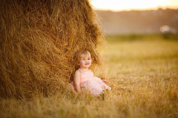 Niño niña sentarse cerca de pila de heno en pendiente campo . —  Fotos de Stock